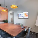 Nowoczesna sala konferencyjna z dużym stołem, ekranem TV i tablicą suchościeralną.