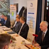 Ludzie siedzący przy stole podczas spotkania, na ścianie banery "Lubelska Izba Rolnicza" i "TUW Ubezpieczenia".