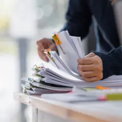 Dłonie przeglądające stosy dokumentów z kolorowymi spinaczami.